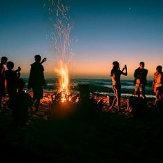 people standing around a campfire at the beach