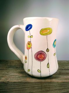 a white coffee mug with colorful flowers painted on the outside and inside, sitting on a wooden table