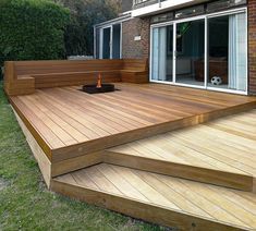 a wooden deck with steps leading up to an outside fire pit in front of a brick building