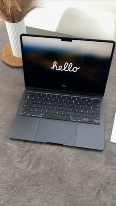 an open laptop computer sitting on top of a table next to a vase with flowers