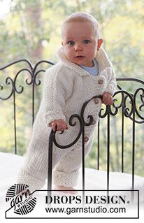 a baby standing on top of a bed next to a metal railing and looking at the camera