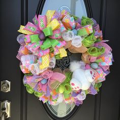 a colorful wreath is hanging on the front door with an easter bunny stuffed animal in it