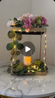 a white marble table topped with a candle and flower arrangement on top of it, surrounded by greenery