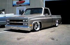 a silver truck parked in front of a building with other cars behind it and another car next to it