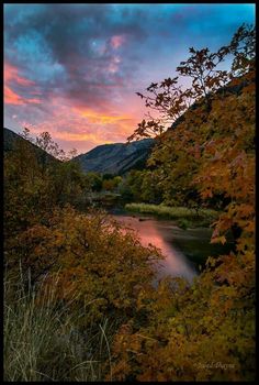 the sun is setting over a river and mountains