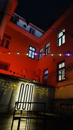 an orange building lit up at night with lights on the windows and below it is a bench