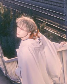 a young man standing next to a train track with a dog on his shoulder and wearing a cape over his shoulders