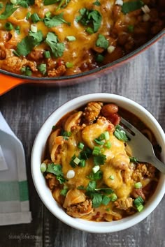 a white bowl filled with chili and cheese next to a fork on top of a wooden table