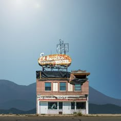 an old brick building with a neon sign on the roof and mountains in the background