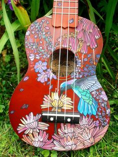 a colorful guitar sitting in the grass with flowers on it