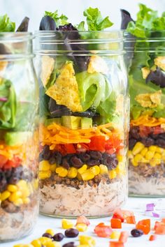 four mason jars filled with different types of salads and toppings on a table