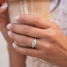 a woman's hand holding a coffee cup with her engagement ring on top of it