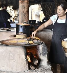 a woman standing in front of an open fire pit with pots on top of it