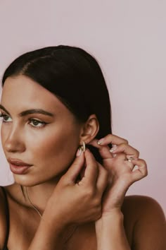 a woman is holding her ear up and looking at the camera while wearing gold jewelry