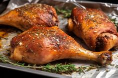 two chicken legs covered in herbs and seasoning on a baking sheet with tin foil