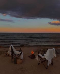 two chairs sitting next to each other on top of a sandy beach near the ocean