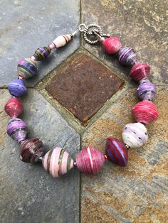 a multicolored bracelet is sitting on a stone floor next to a piece of metal