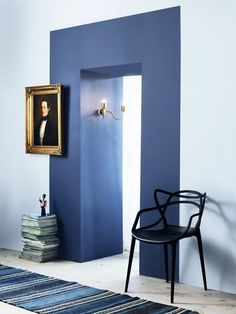 a blue room with a black chair and a painting on the wall next to it