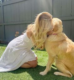 a woman kneeling down next to a dog on top of a lush green field,