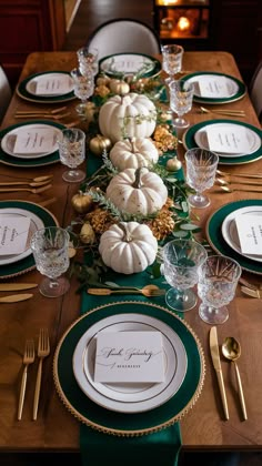 the table is set with white pumpkins, greenery and gold place settings for dinner