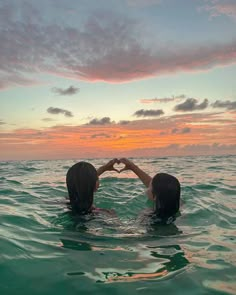 two people in the water making a heart with their hands