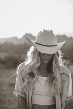 a woman wearing a cowboy hat standing in the middle of a field with her hands on her hips