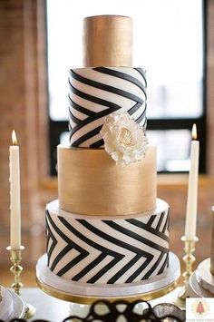 a three tiered cake decorated with black and white stripes, gold accents and flowers