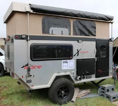 an off - road camper parked in the grass with people standing around looking at it