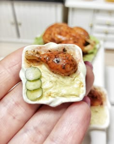 a hand holding a miniature food dish with cucumbers and shrimp on it's side