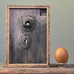 an egg sitting in front of a wooden frame with a lock on it next to a brown egg