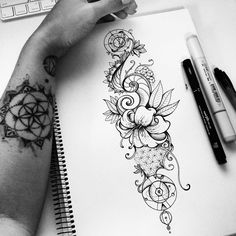 a woman's hand holding a pen and drawing flowers on a notebook next to a keyboard