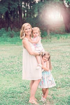 a mother and her two daughters posing for a photo in the grass with trees in the background