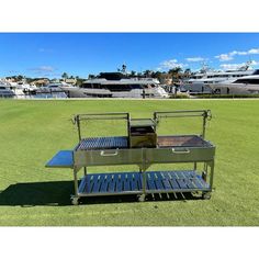 an outdoor grill on the grass with boats in the background