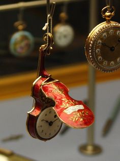 an old clock hanging from a chain with a red shoe on it's side