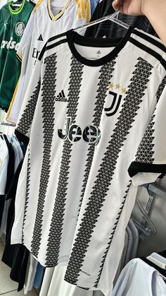 a person holding up a soccer jersey in front of several other shirts hanging on racks