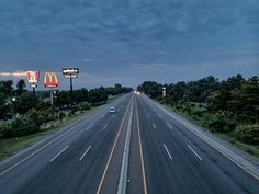 an empty highway at dusk with cars driving on it and mcdonald's sign in the distance