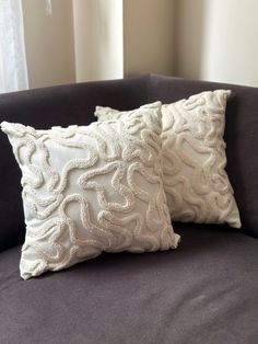 two white pillows sitting on top of a gray couch in front of a windowsill