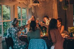 a group of people sitting around a table with wine glasses in their hands and candles lit