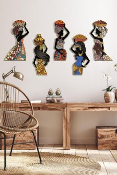 four african women are hanging on the wall next to a wooden table with a wicker chair