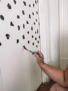 a person holding a pair of scissors in front of a wall with black paint on it