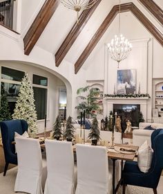 a dining room table with white chairs and christmas trees on the tables in front of it