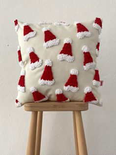 a pillow with santa hats on it sitting on a wooden stand in front of a white wall