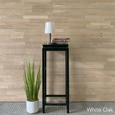 a small black table with a lamp on it next to a potted plant in front of a wood paneled wall