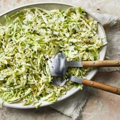 a white bowl filled with shredded cabbage next to two wooden spoons on top of a table