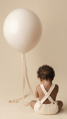 a baby sitting on the ground with a balloon in the air