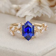 a blue and white diamond ring sitting on top of a cushioned surface next to flowers