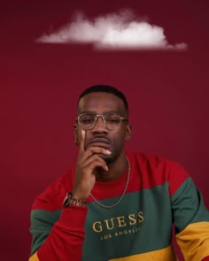 a man sitting in front of a red wall with a cloud above his head