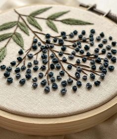 a close up of a embroidery on a wooden hoop with blue beads and green leaves