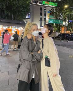 two women standing on the sidewalk wearing face masks