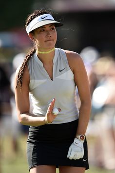 a woman holding a golf ball in her right hand and wearing a white visor